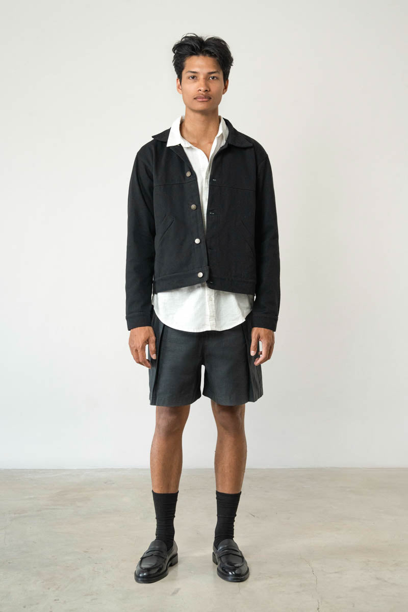 Man wearing a black jacket, white shirt, and black shorts on a plain background