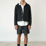 Man wearing a black jacket, white shirt, and black shorts on a plain background